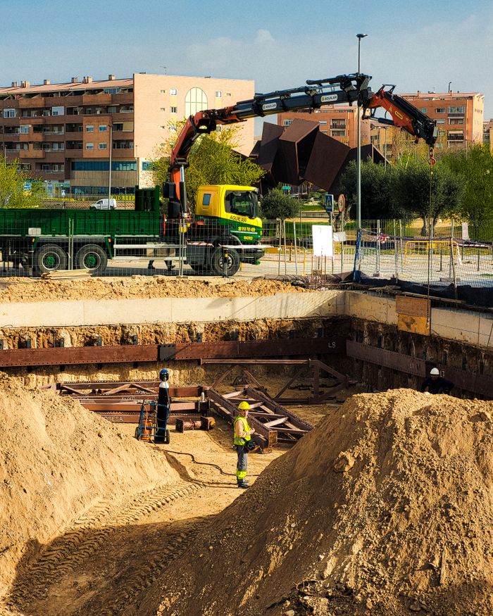 Construction workers operating at an urban site in Madrid, with machinery and residential buildings in view.
