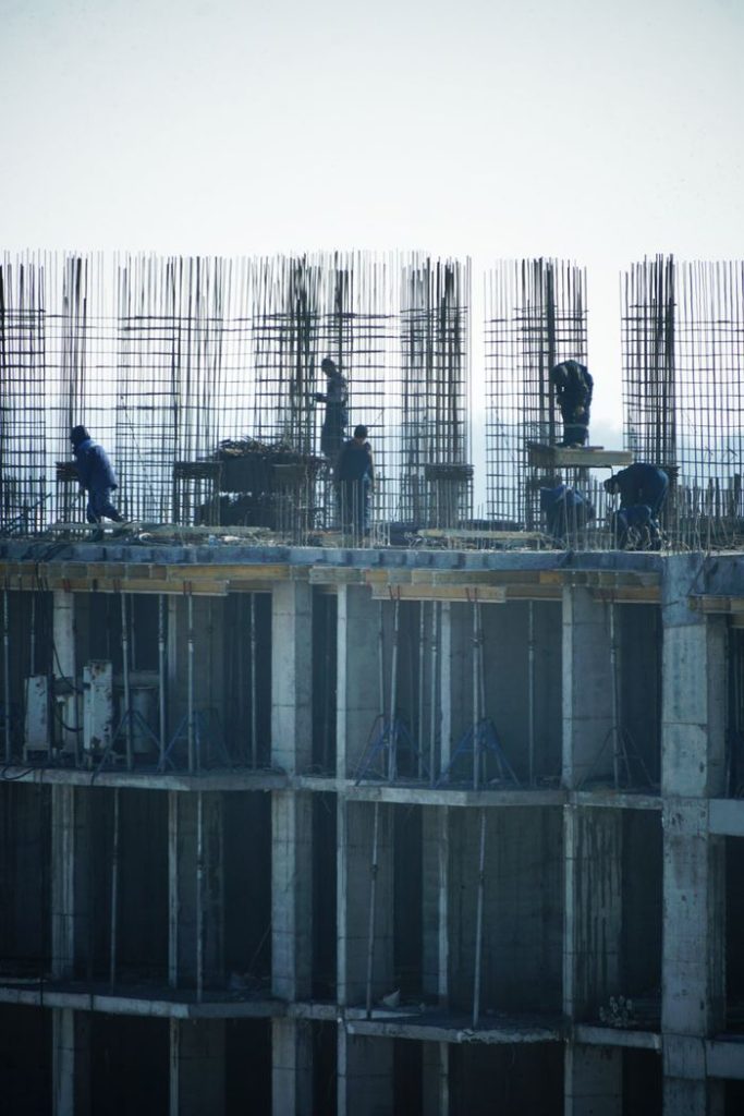 Construction workers at a high-rise building site with visible steel reinforcements.